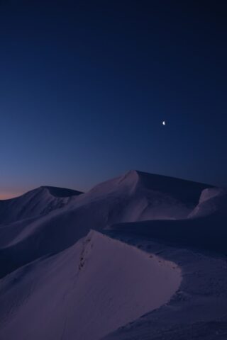 Snowy mountain range under a dark blue twilight sky.